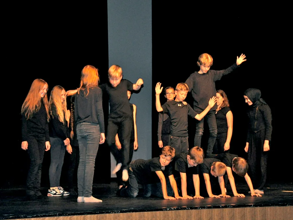 Darsteller in Schwarz bilden auf der Bühne eine Formation.